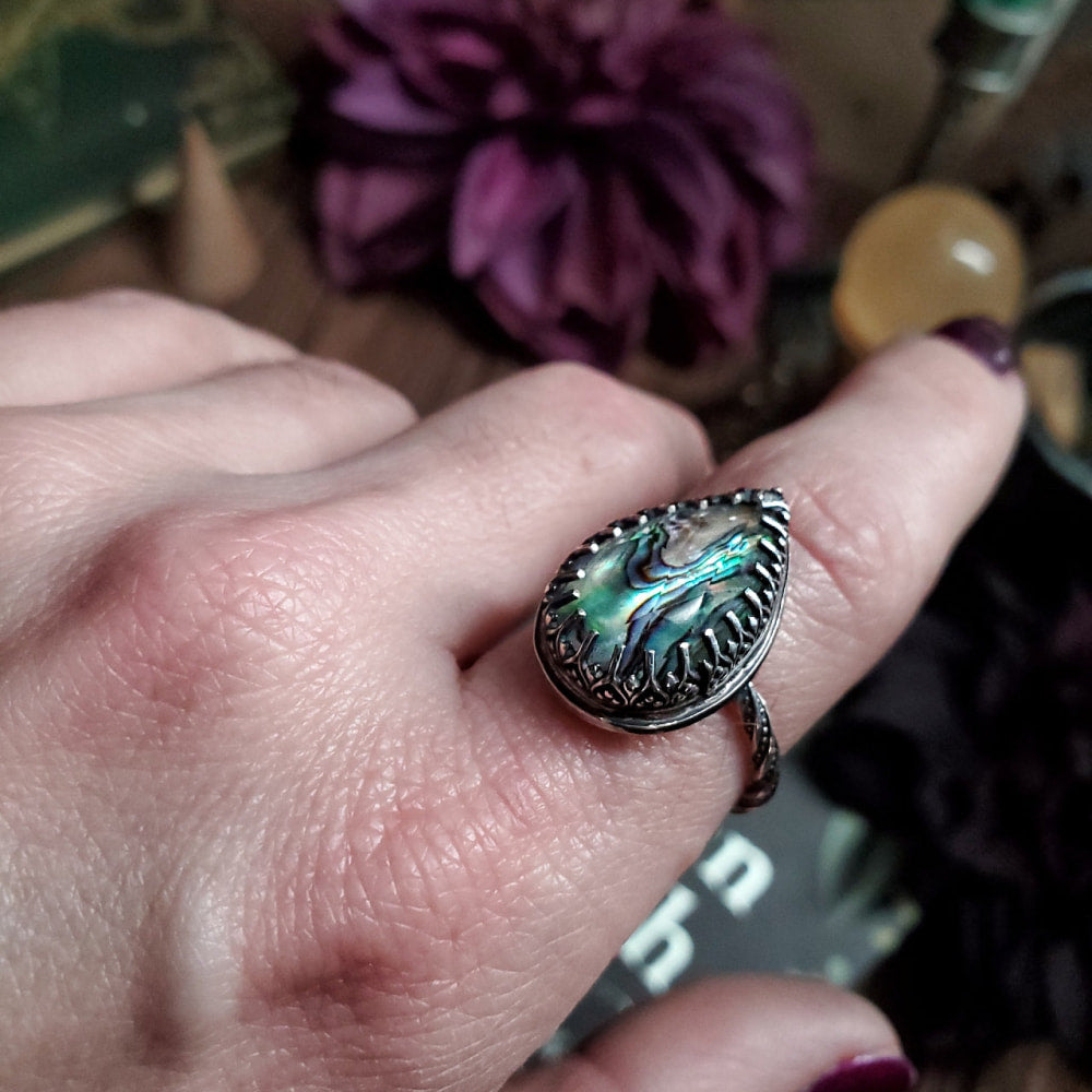 a woman’s hand holding a ring with a green and blue stone
