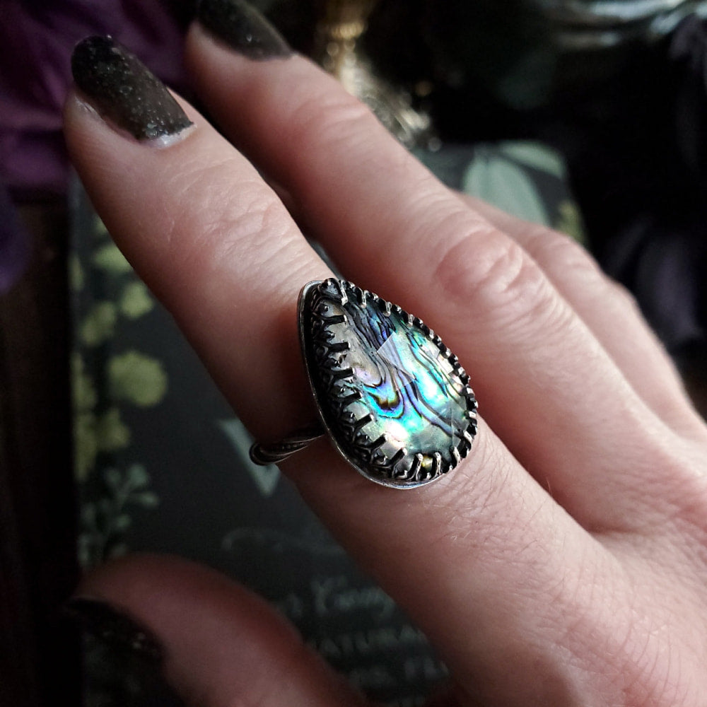 someone is holding a ring with a blue and green stone