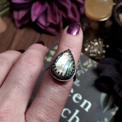 a woman’s hand holding a ring with a rainbow colored stone