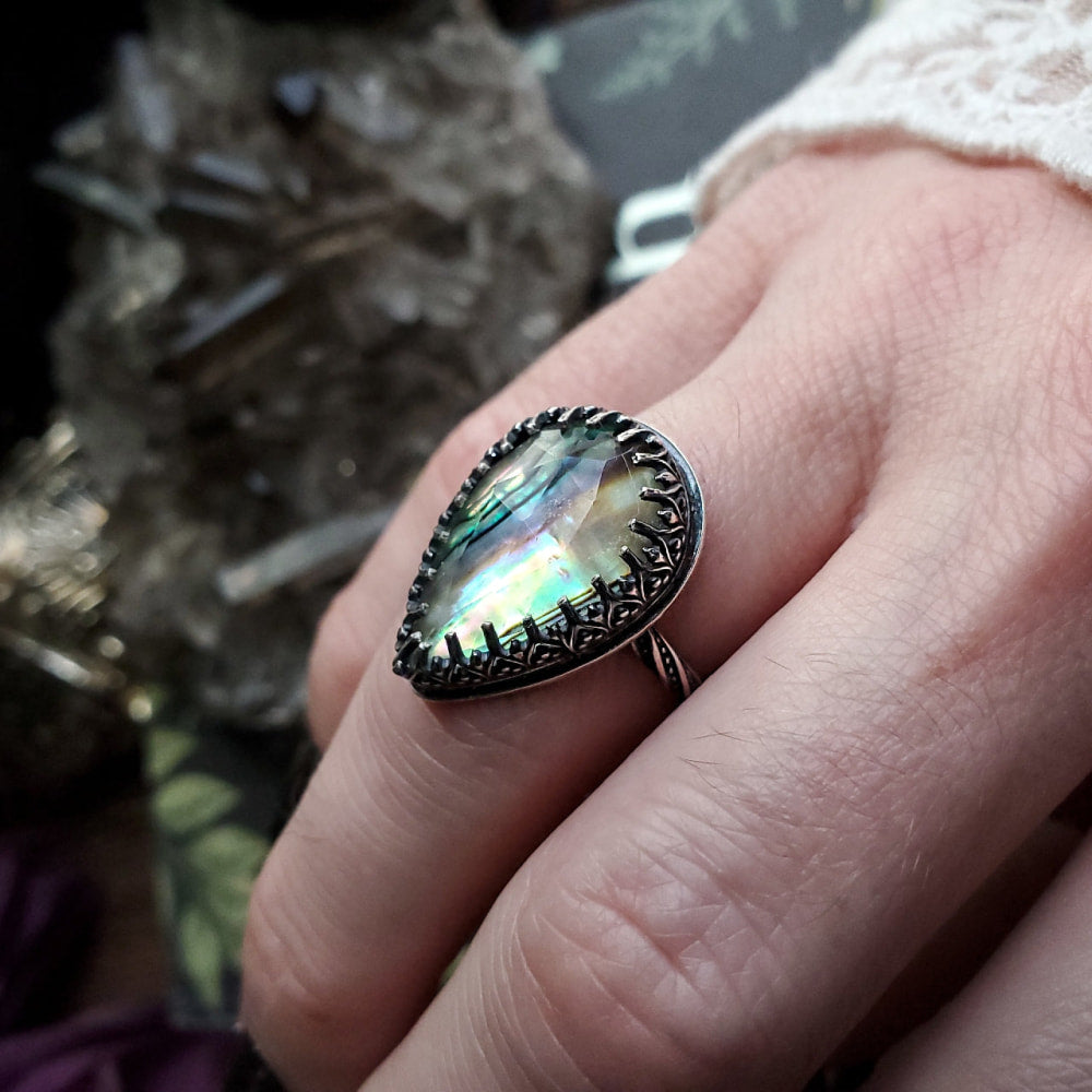 a woman’s hand holding a ring with a rainbow colored stone