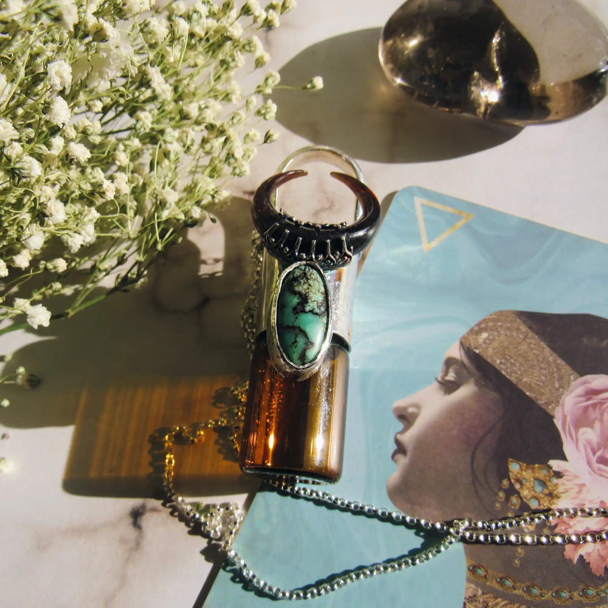 An amber glass roller bottle adorned with a silver ring featuring a turquoise stone and a dark, crescent-shaped top.