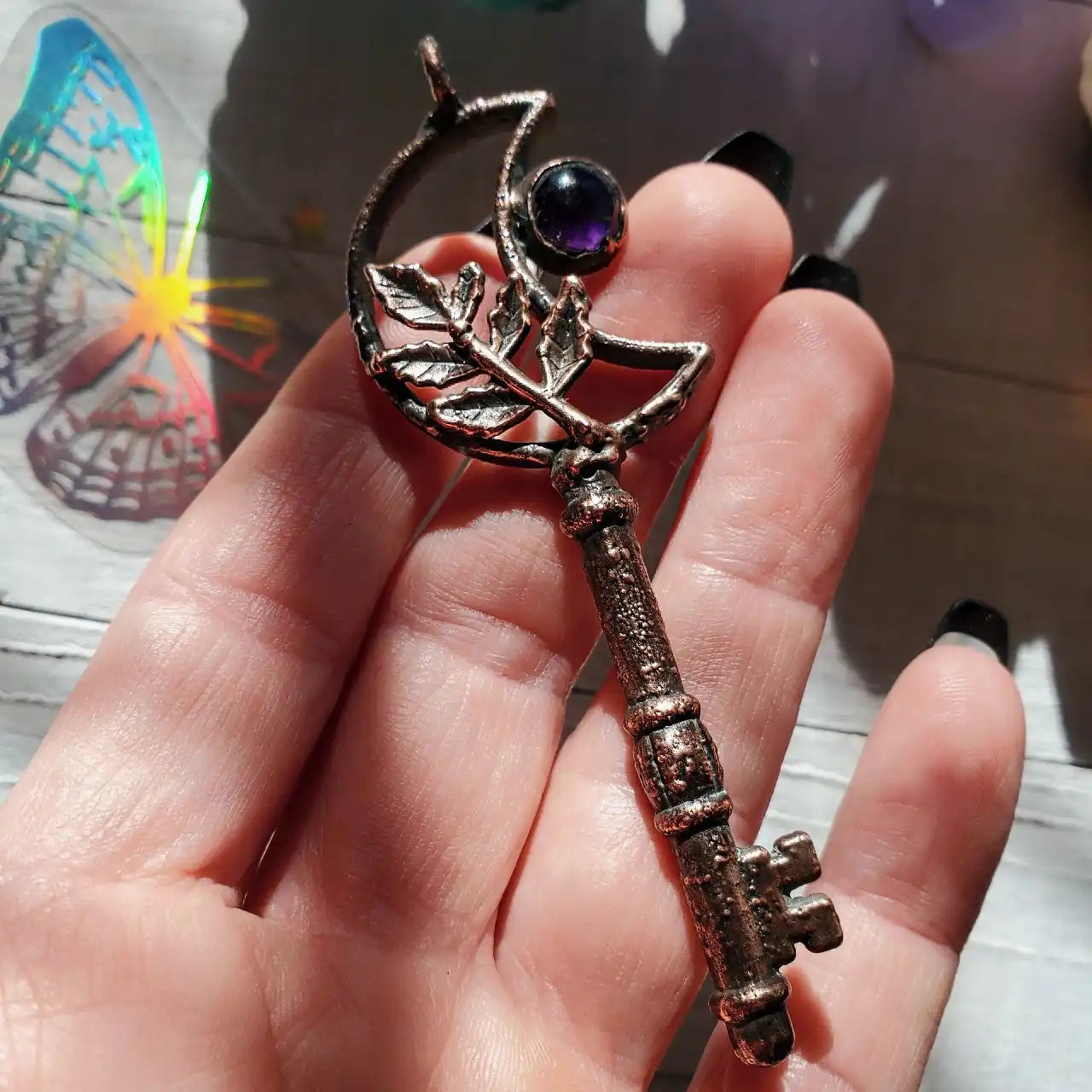 An antique-style bronze key with a crescent moon and leaf design, adorned with a purple gemstone.