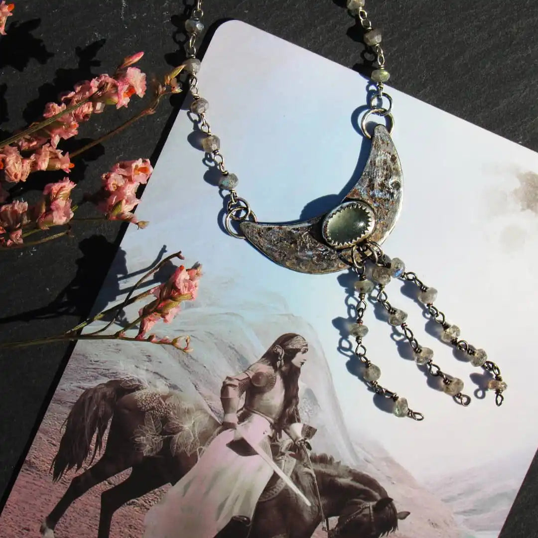 A crescent moon-shaped silver necklace with a light green gemstone and multiple dangling beaded chains.