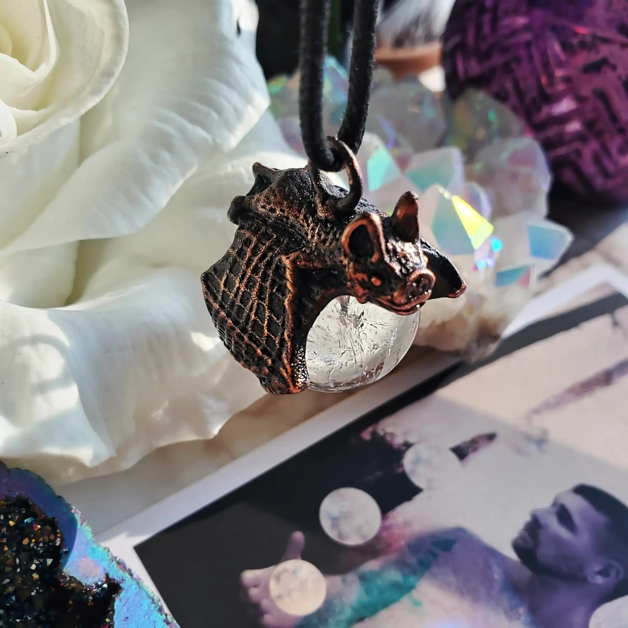 A dark bronze-colored bat necklace with a clear, spherical crystal.