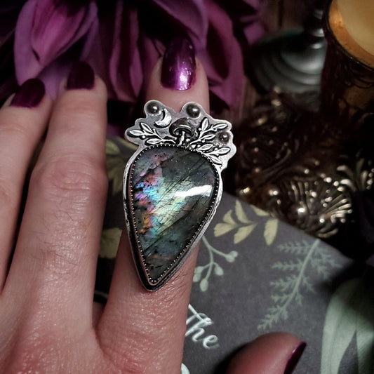 someone is holding a ring with a heart shaped stone on it