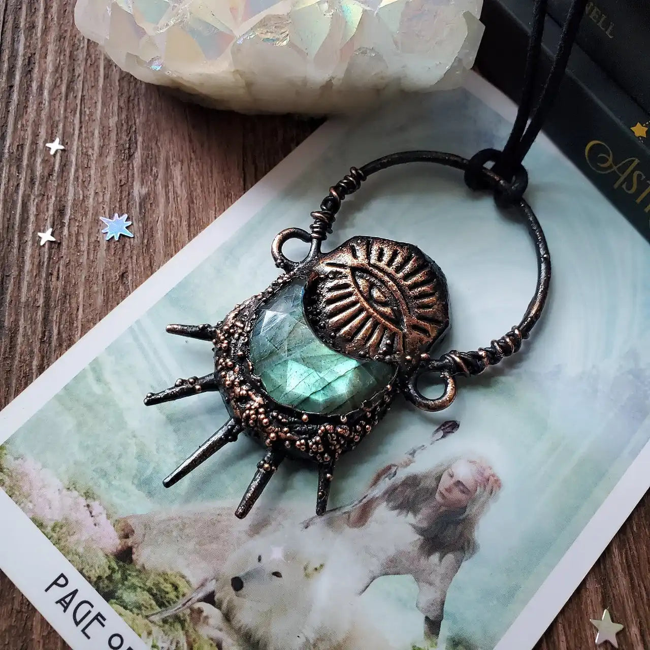 A dark metal pendant with a central iridescent green gemstone and an etched eye design.