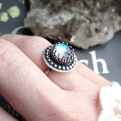 a person holding a ring with a rainbow colored stone