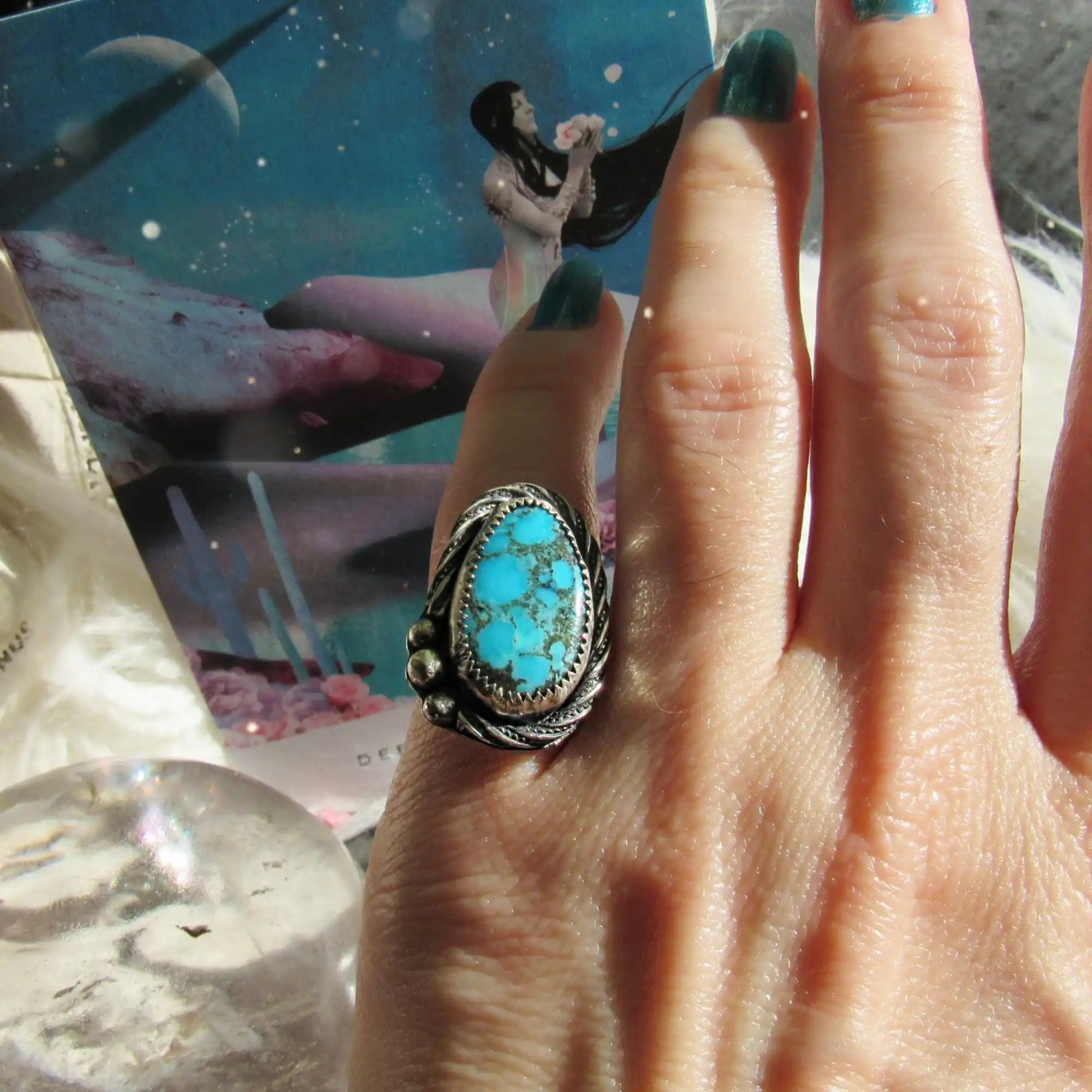 A hand adorned with a silver ring featuring an oval turquoise stone.