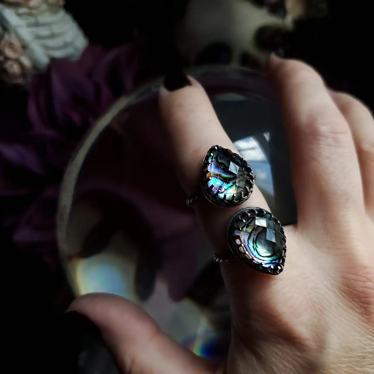 A hand wearing two teardrop-shaped rings with iridescent abalone shell inlays.