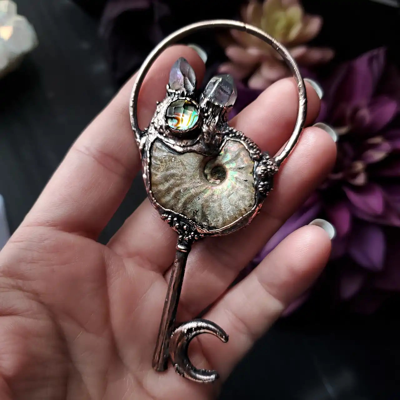 A handcrafted copper key pendant featuring a prominent ammonite fossil, iridescent abalone, and two raw crystal points.