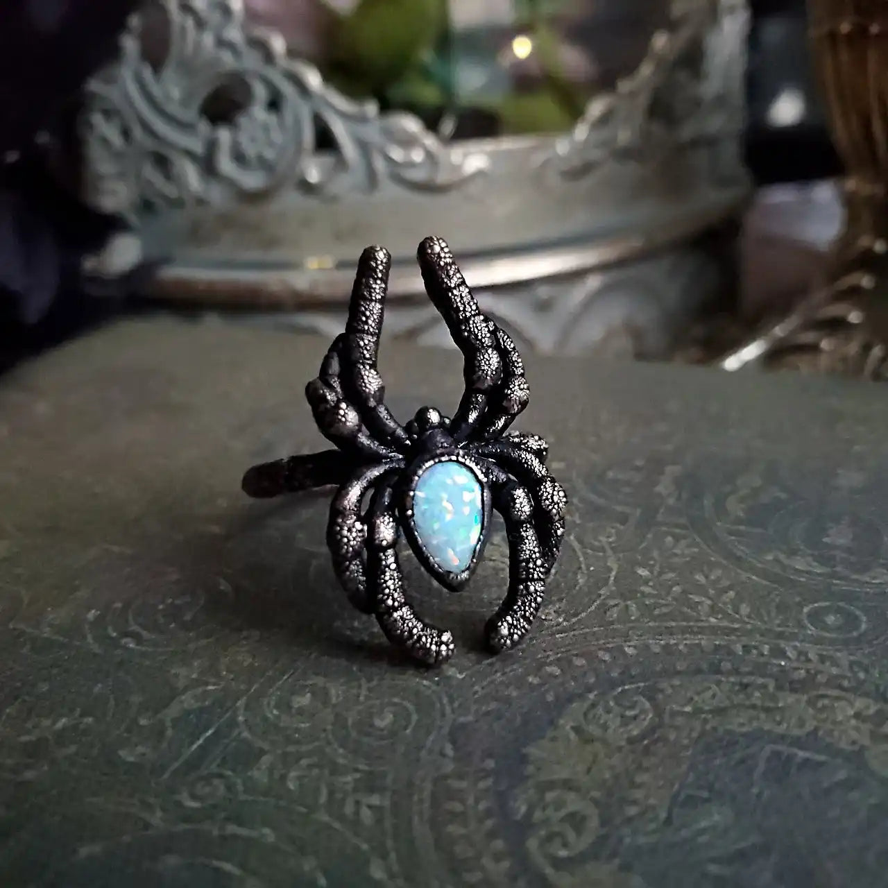 An intricate spider-shaped ring with an iridescent light blue center stone.