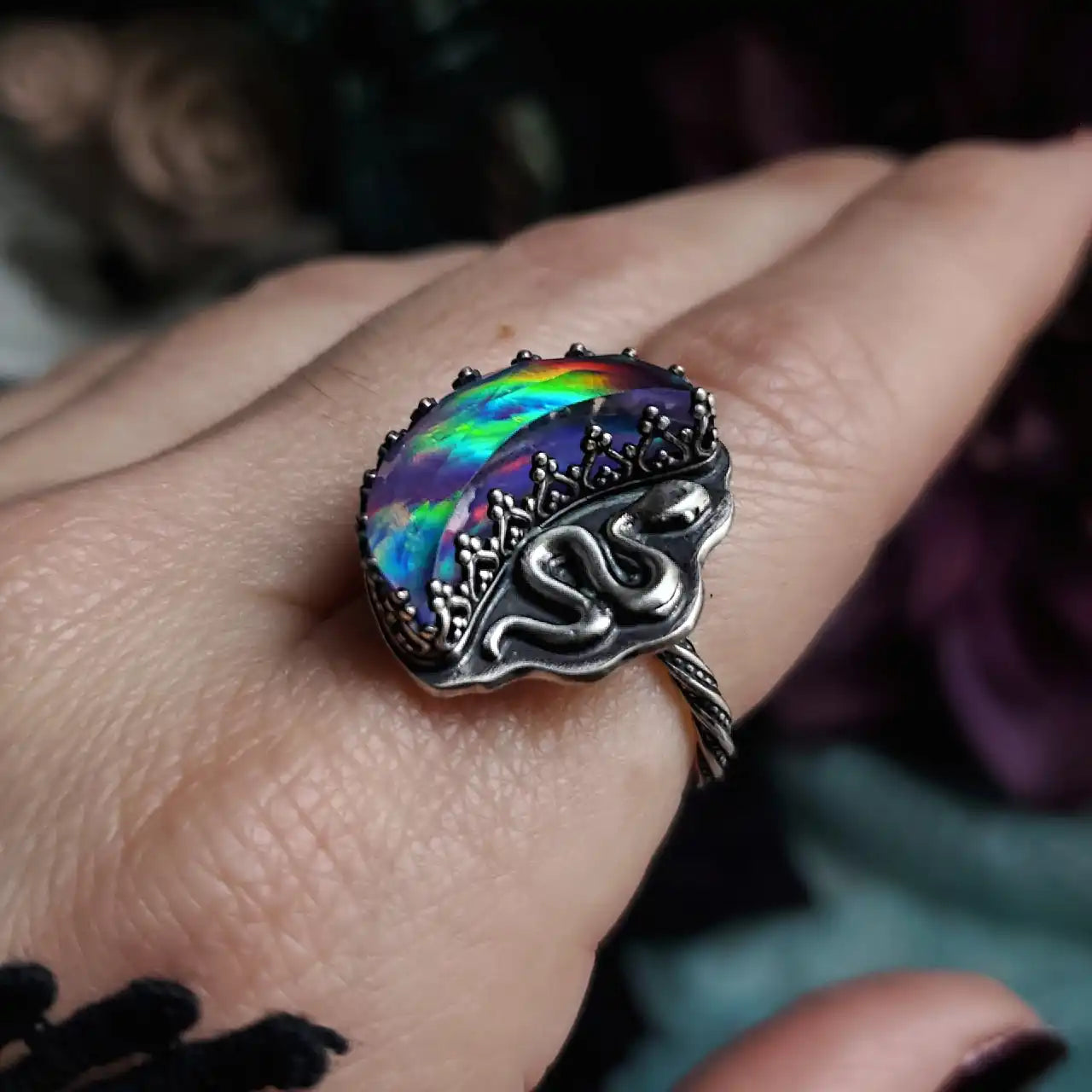An iridescent, oval-shaped ring featuring a silver snake design and a textured band.