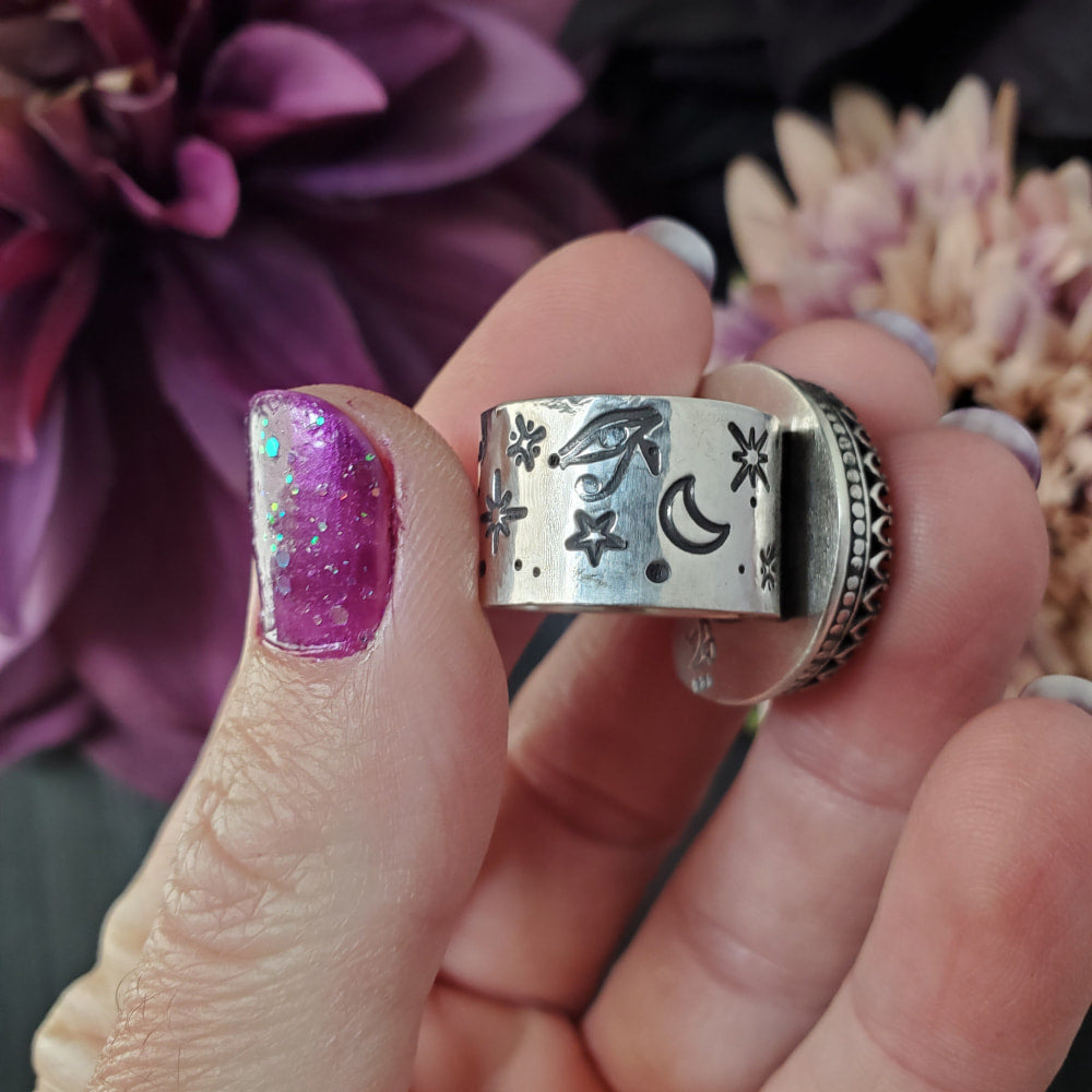 a woman’s hand holding a silver ring with a purple flower