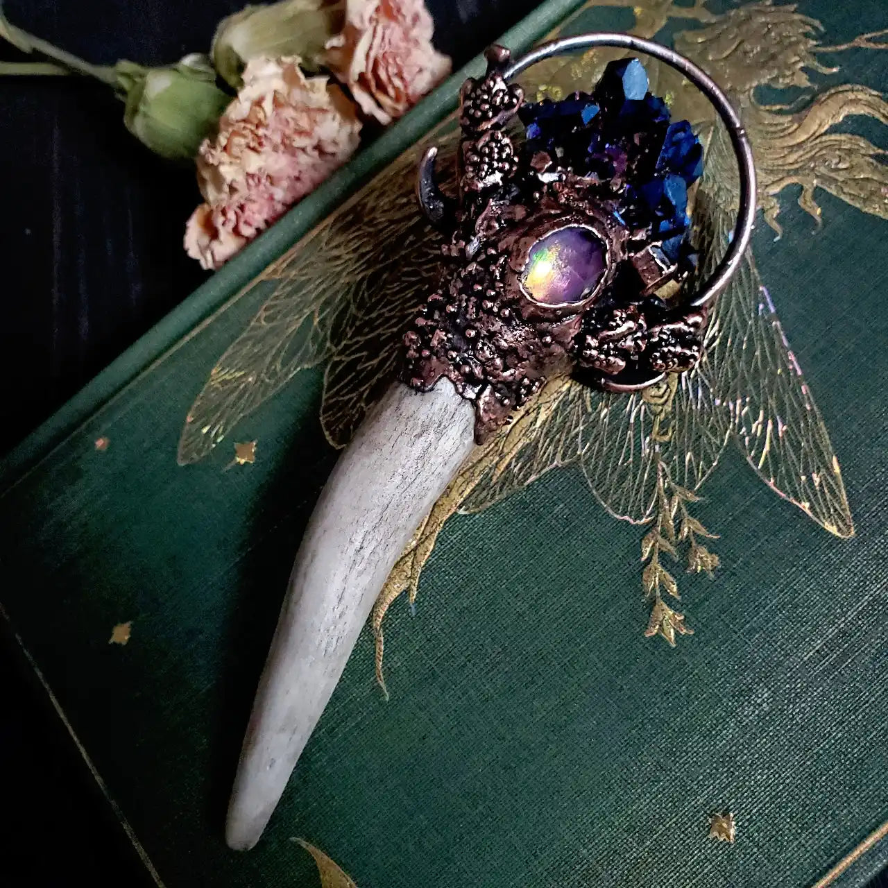 An ornate antler pendant featuring dark blue crystals and an iridescent purple cabochon.