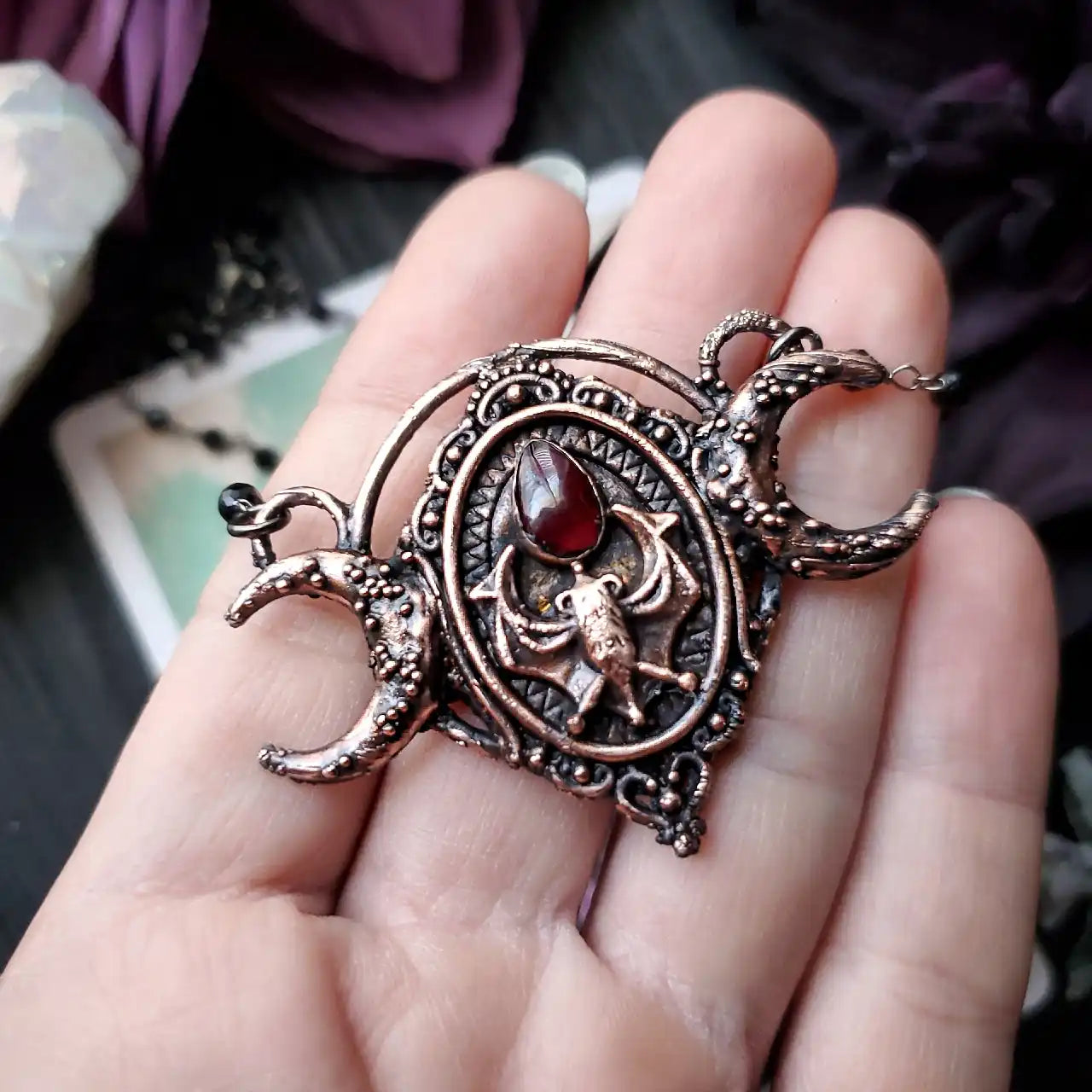 Ornate copper pendant featuring a central spider motif with a red gemstone, flanked by two crescent moons.