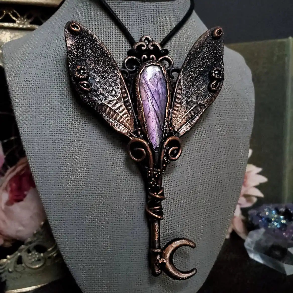 An ornate, dark bronze-toned fairy wing key necklace with a central purple moonstone cabochon and a crescent moon key end.