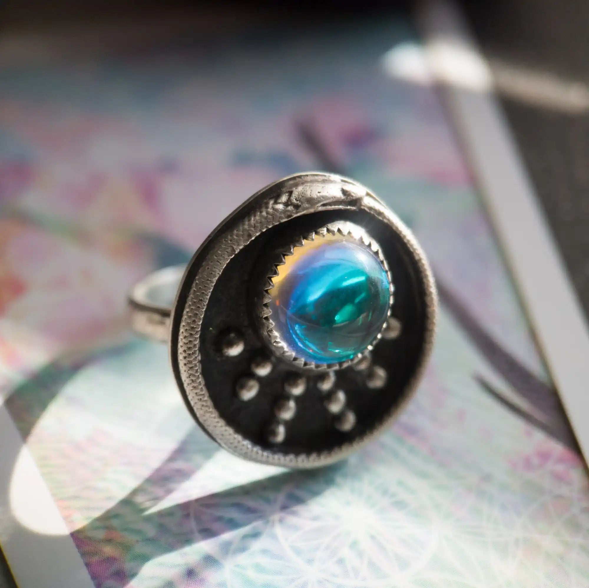An ornate sterling silver ring with a luminous, iridescent blue-green cabochon stone and a snake motif.