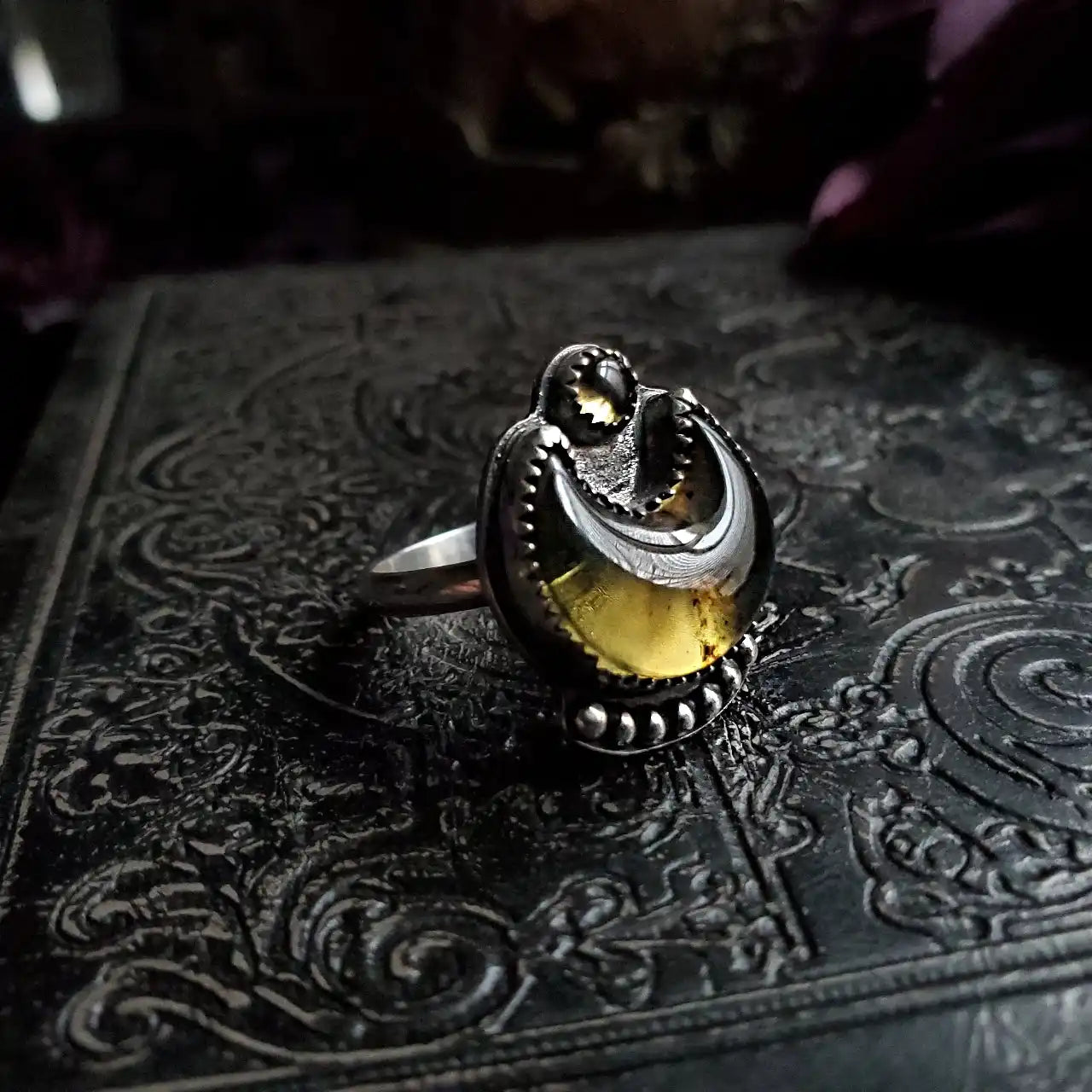 An ornate silver ring with a yellow-green gemstone.