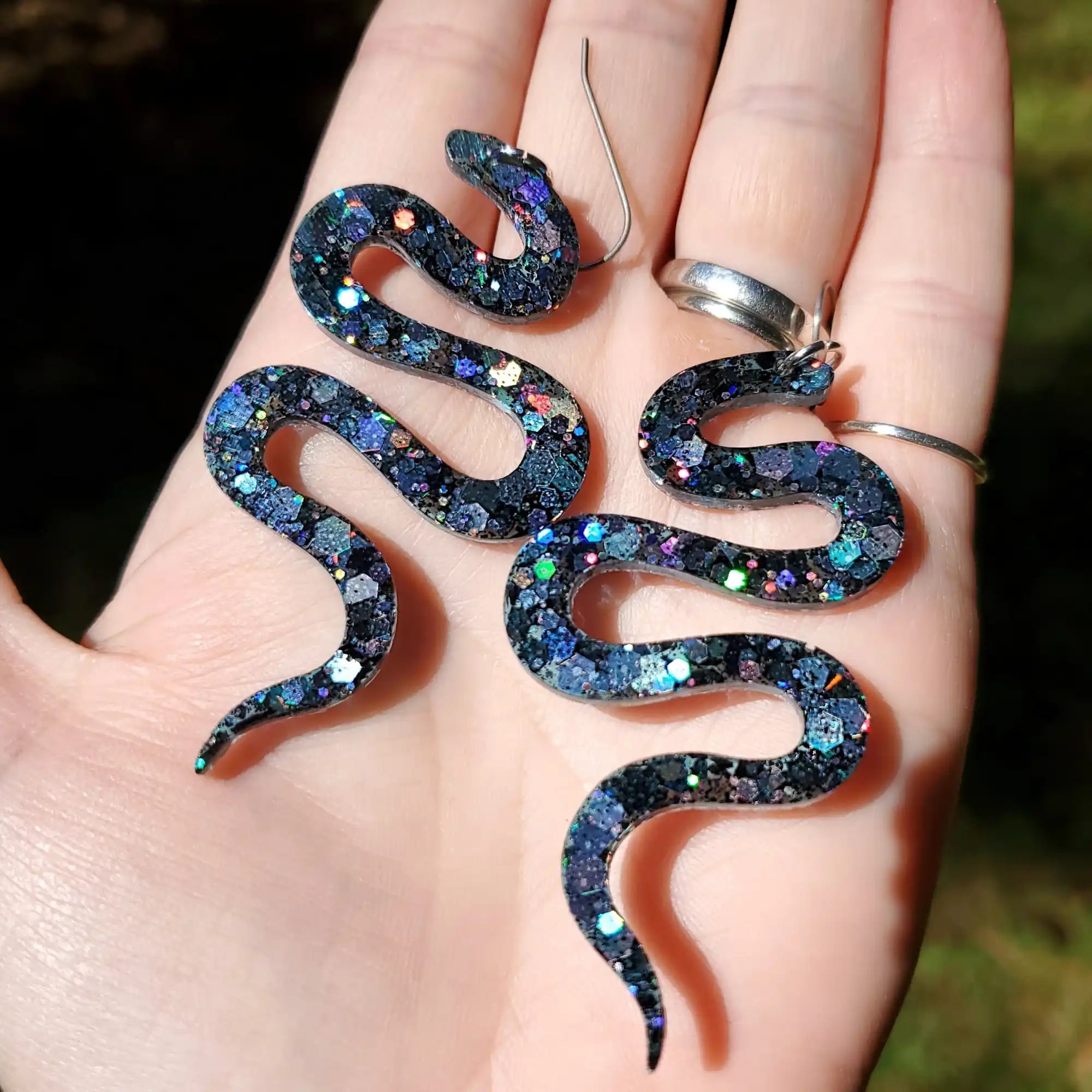 A pair of dark, glittery, snake-shaped dangle earrings.
