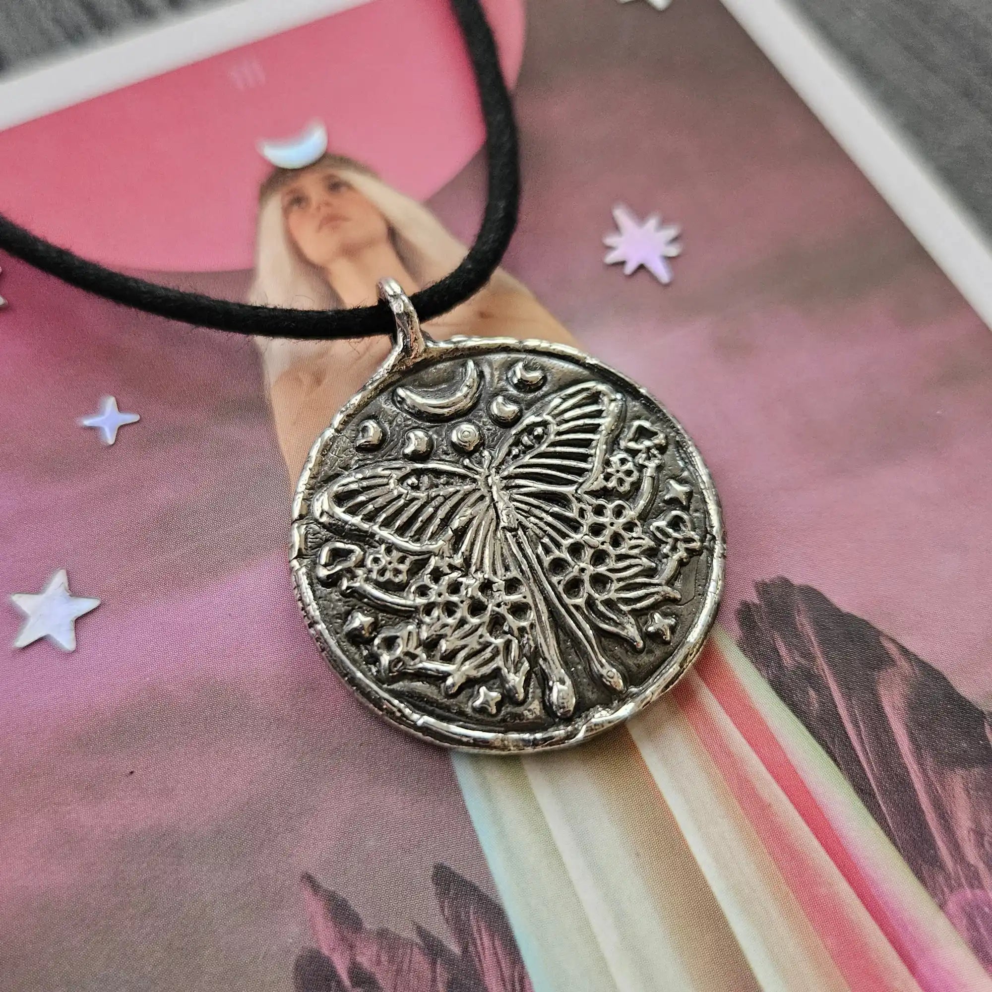 A round, silver-toned pendant with an engraved butterfly design on a black cord necklace.