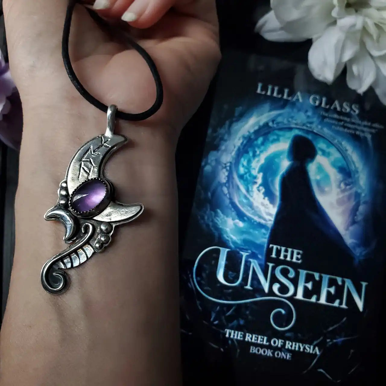 Silver crescent moon pendant with a purple gemstone.