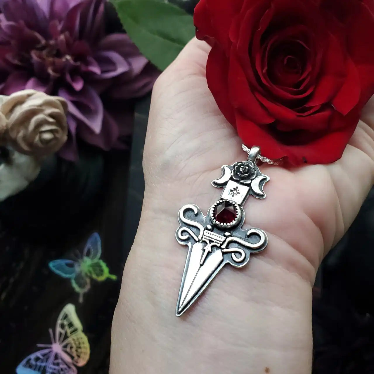 Silver dagger pendant with a red gemstone, featuring crescent moons and a rose design.