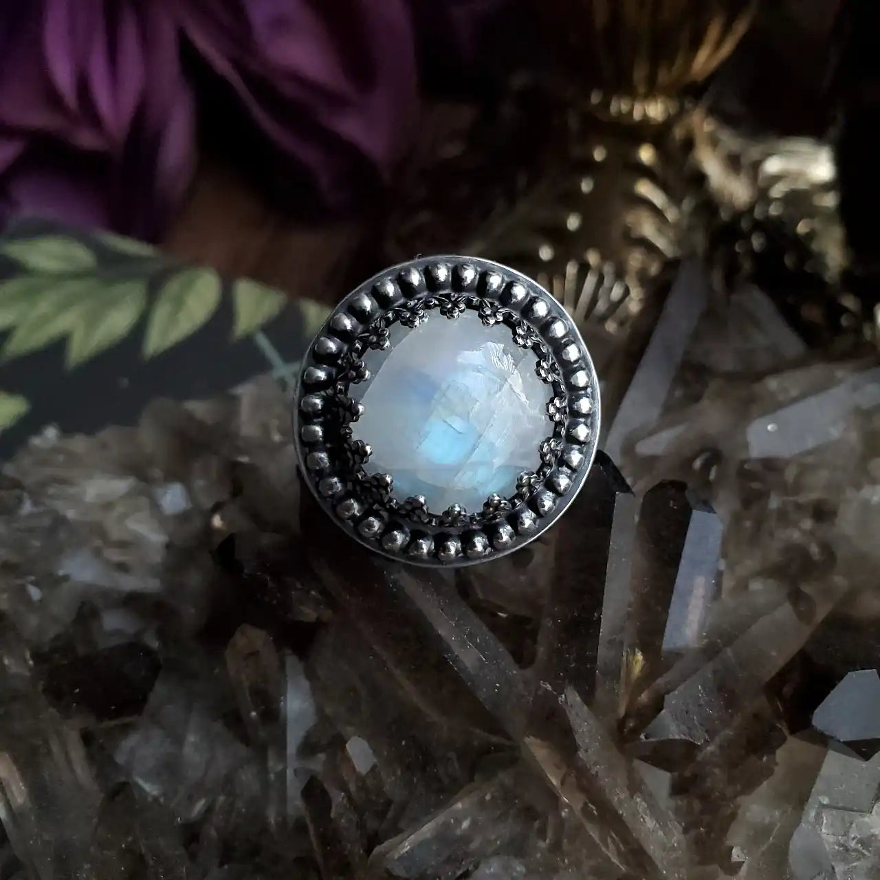 A sterling silver ring featuring a faceted, iridescent moonstone cabochon set in a decorative bezel with beaded accents.