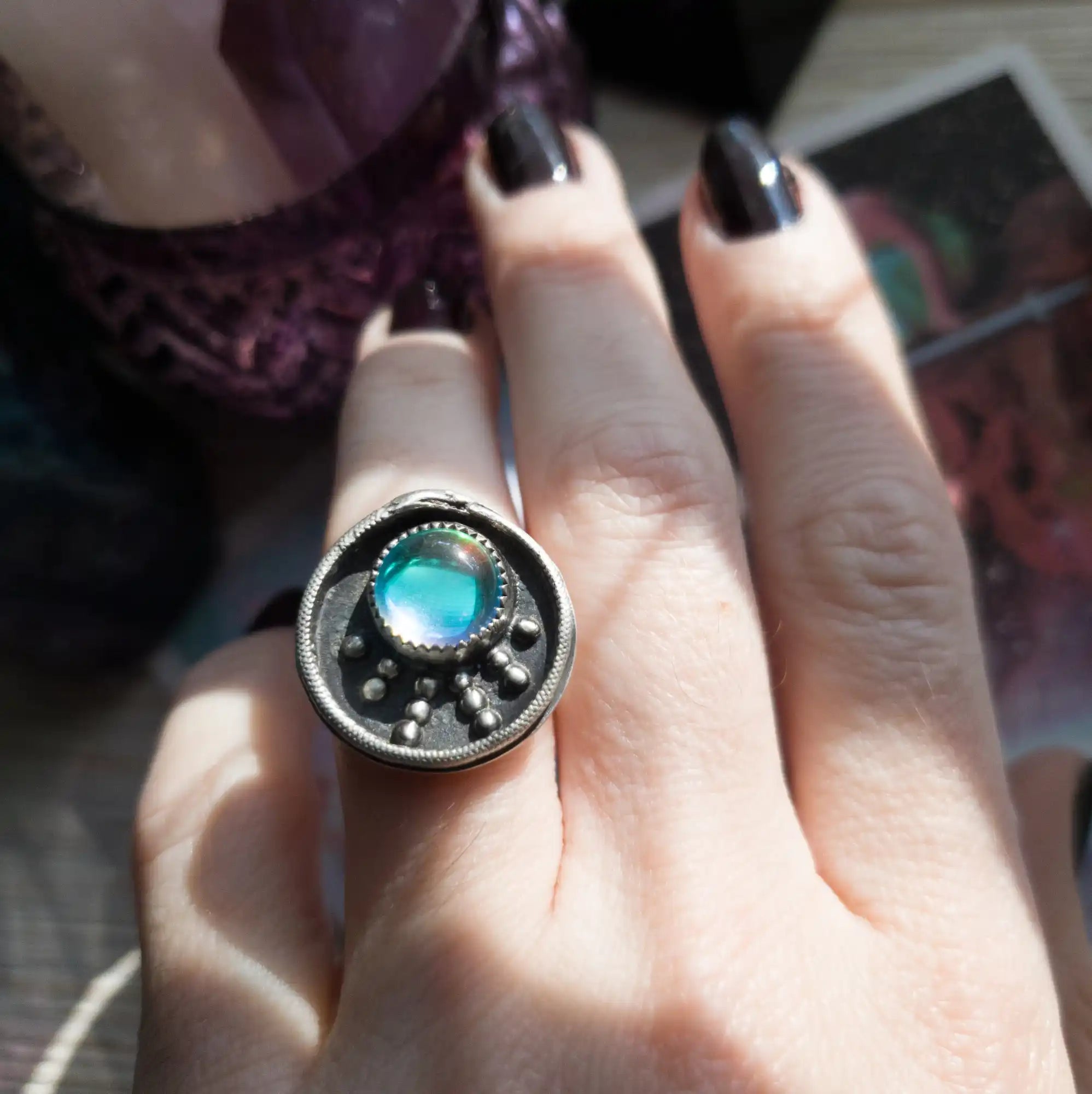A silver ring with a round, iridescent blue-green stone and small raised dots.