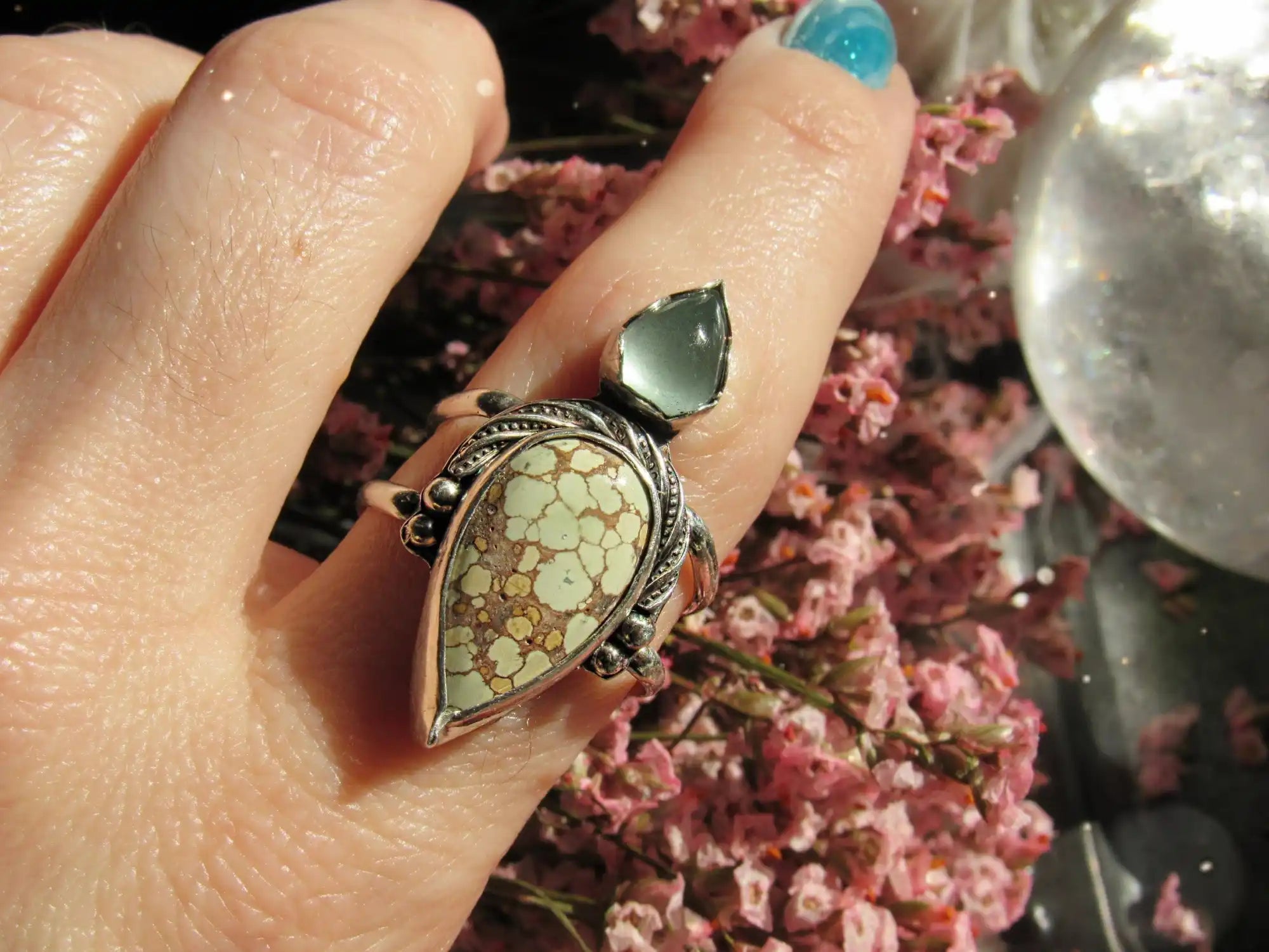 A silver ring with a teardrop-shaped light green turquoise stone with brown matrix, and a smaller, light blue-green faceted stone on top.