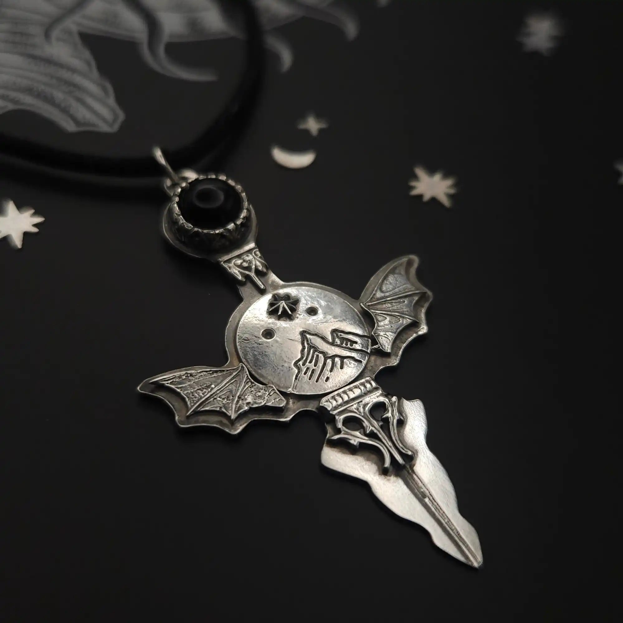 A silver-toned gothic-style pendant featuring a winged skull, a black gem, and a dagger-like base.