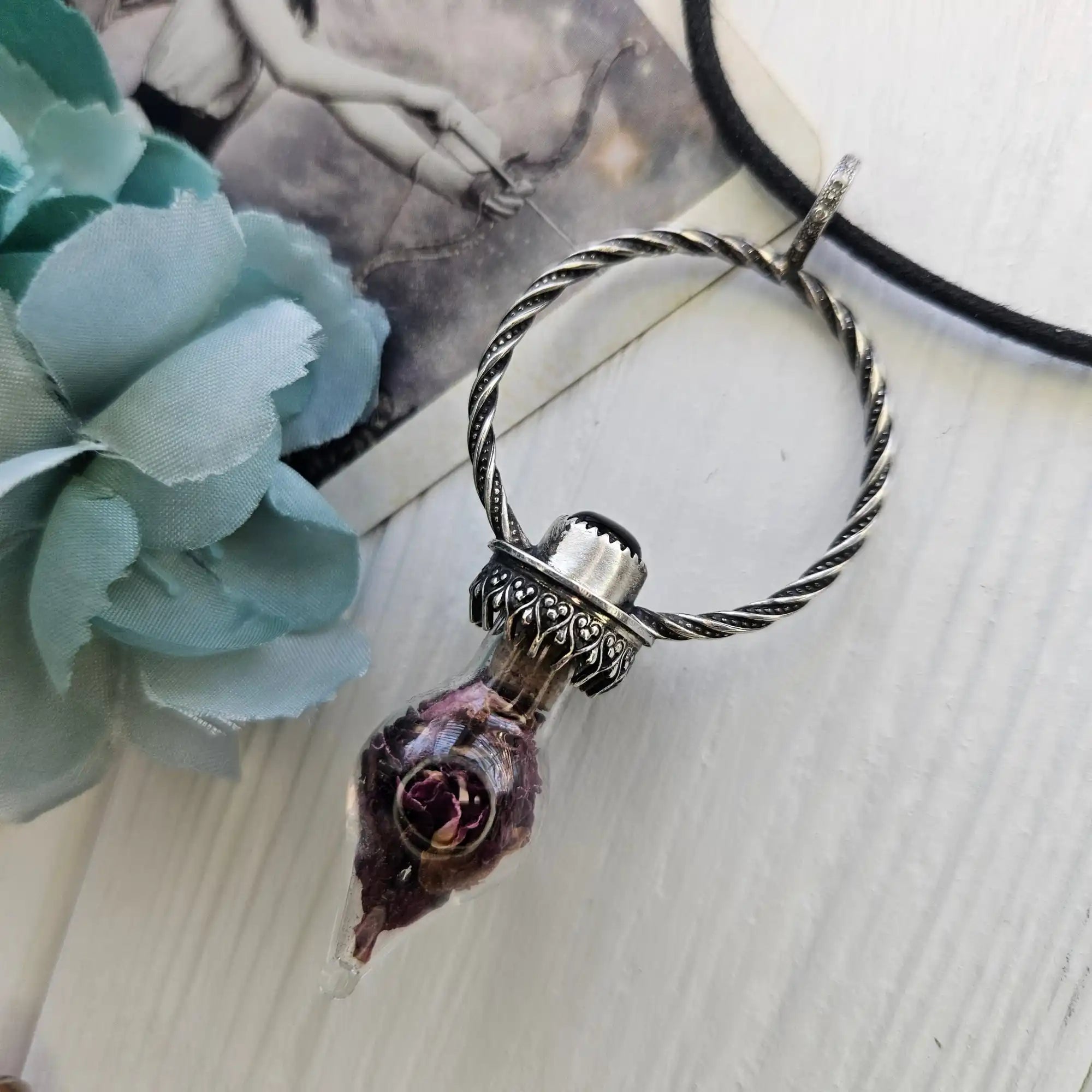 A silver-toned twisted-ring pendant with a glass vial containing dried flowers.